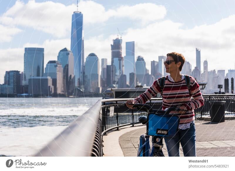 USA, woman with bicycle at New Jersey waterfront with view to Manhattan New York State females women bikes bicycles United States United States of America