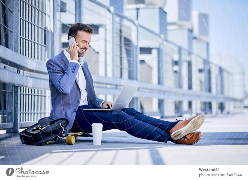 Businessman making phone call and using laptop outdoors smiling smile on the phone telephoning On The Telephone calling sitting Seated skateboard Skate Board