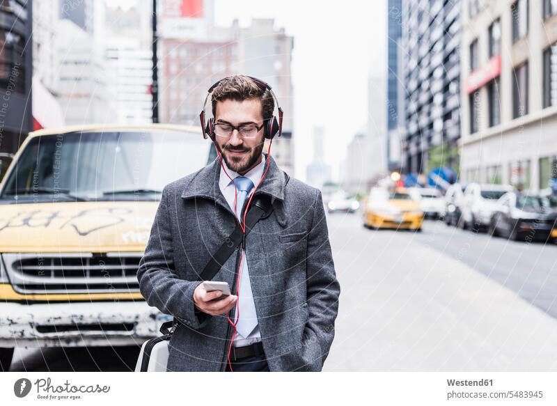USA, New York City, businessman with cell phone and headphones on the go Businessman Business man Businessmen Business men smiling smile males headset