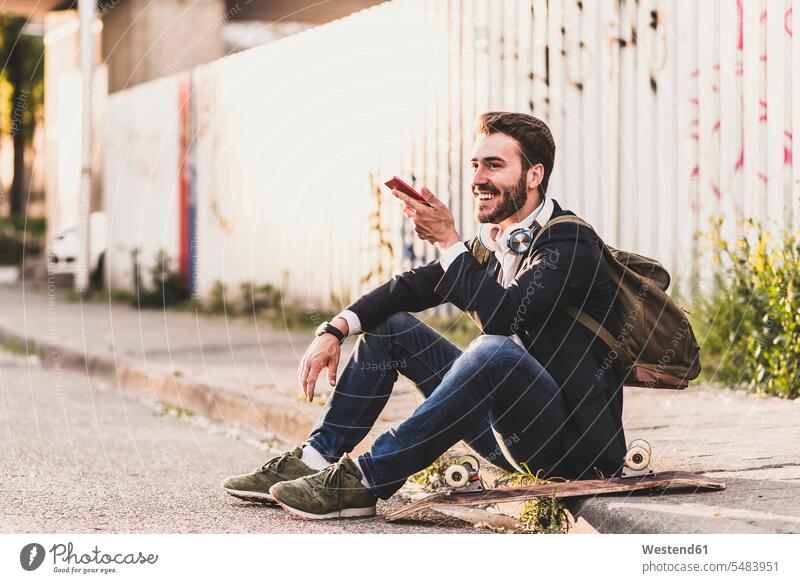 Smiling young man sitting on pavement using cell phone smiling smile mobile phone mobiles mobile phones Cellphone cell phones Seated males telephones
