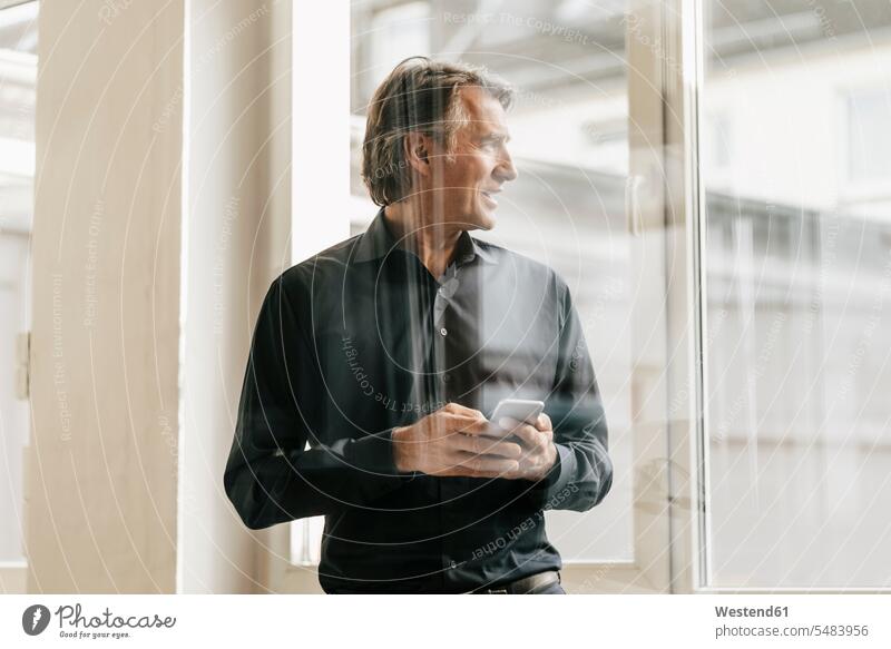 Mature businessman holding cell phone at the window windows mobile phone mobiles mobile phones Cellphone cell phones looking view seeing viewing Businessman
