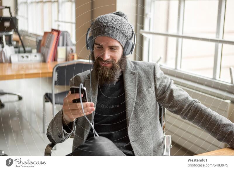Portrait of young businessman wearing beany hat using smart phone men males Hipster Hipsters unconventional Offbeat technology technologies Technological