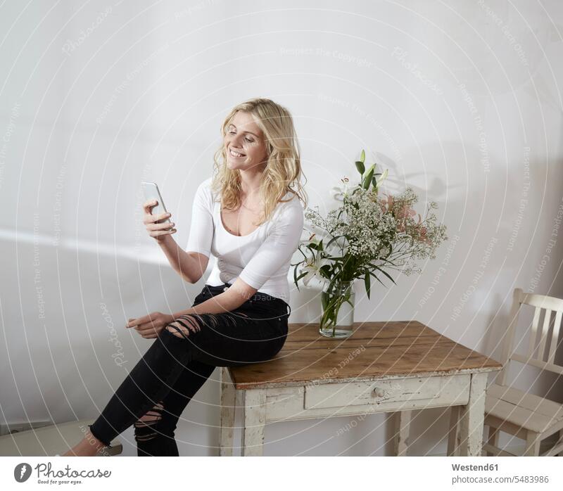 Young woman sitting on an old wooden table looking at her smartphone caucasian caucasian ethnicity caucasian appearance european Seated indoors indoor shot