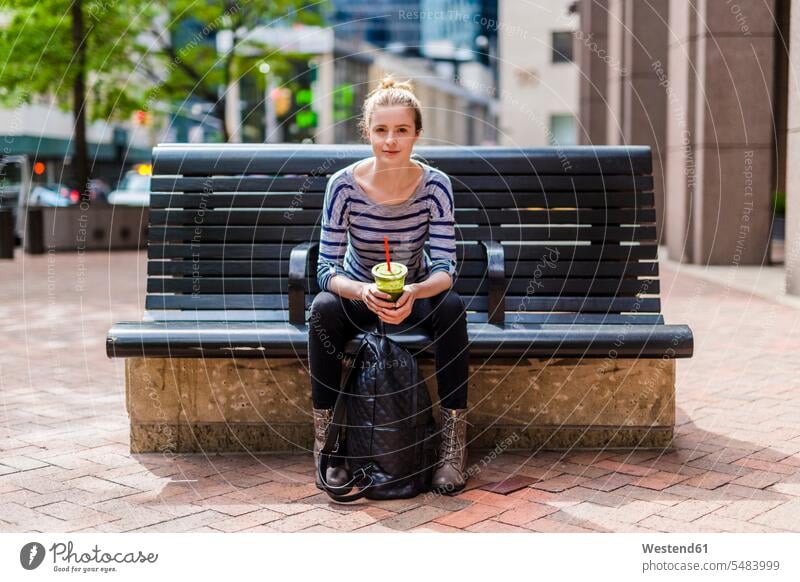 USA, New York City, portrait of woman sitting on a bench drinking a smoothie in Manhattan Seated benches females women Smoothies Adults grown-ups grownups adult