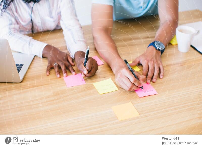 Young man and woman in office writing on adhesive notes on desk desks young entrepreneur young entrepreneurs start-up entrepreneur business people