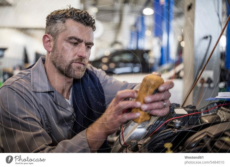 Car mechanic in a workshop using diagnostic equipment car automobile Auto cars motorcars Automobiles mechanician repairman mechanicians mechanists repairmen