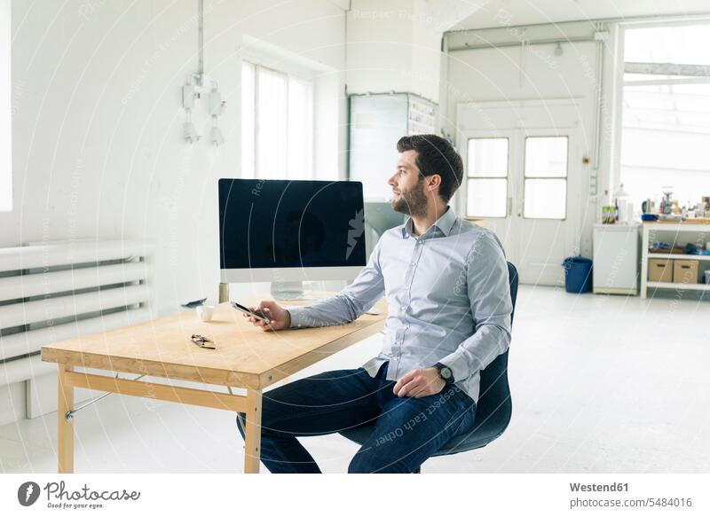 Businessman with cell phone sitting at desk in office mobile phone mobiles mobile phones Cellphone cell phones Seated desks Business man Businessmen