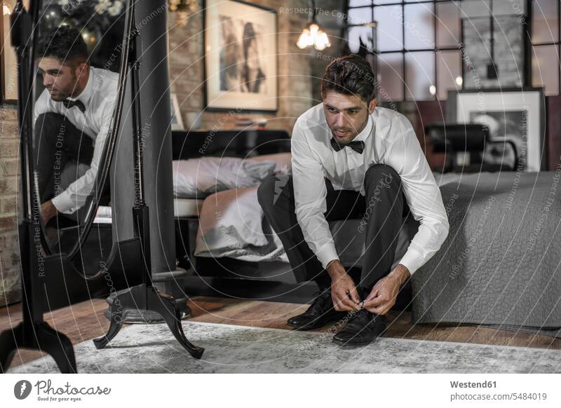 Man sitting on bed tying shoes shirt shirts flat flats apartment apartments well-dressed dressed up mirrored Reflected mirroring white shirt cultivated tie