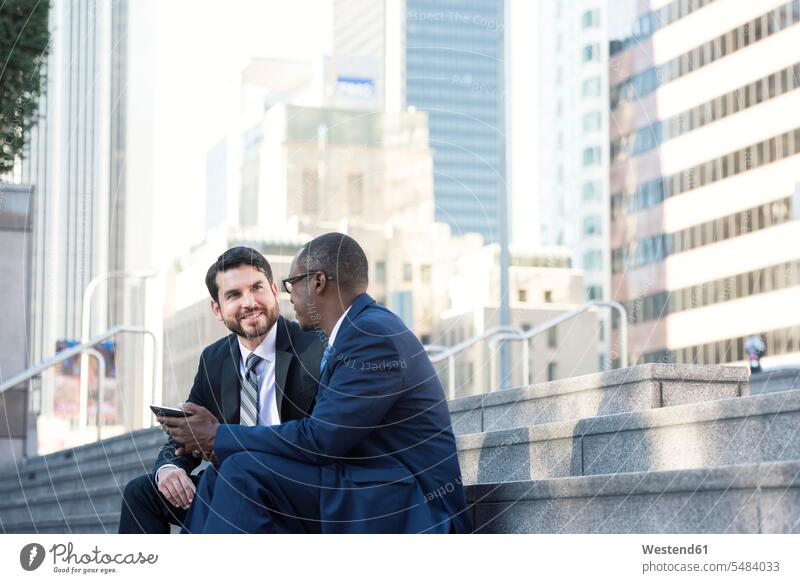 Two businessmen sitting on stairs talking and sharing tablet speaking Businessman Business man Businessmen Business men colleagues digitizer Tablet Computer