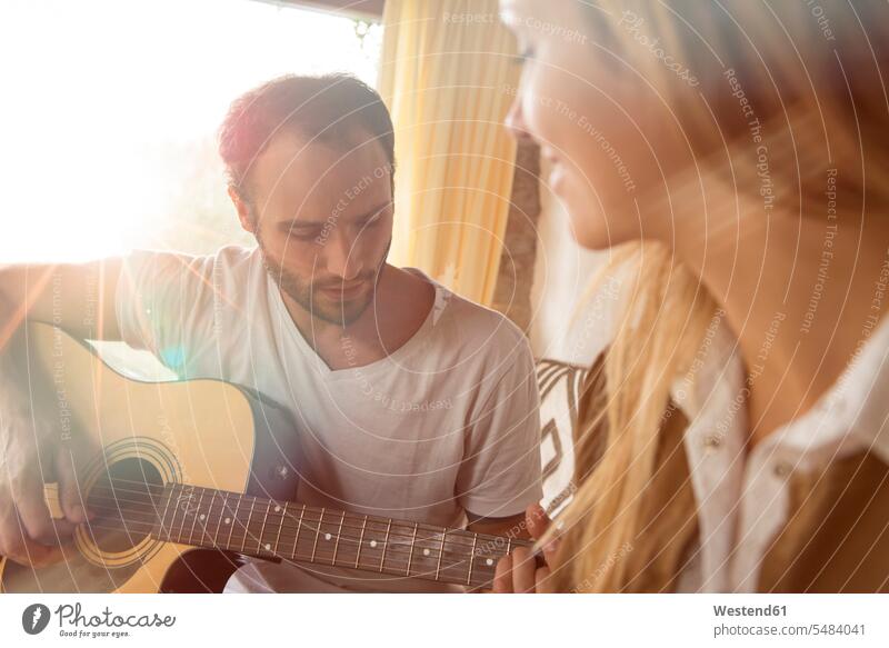 Man playing guitar at home while his girlfriend watching him making music playing music make music play music man men males Adults grown-ups grownups adult
