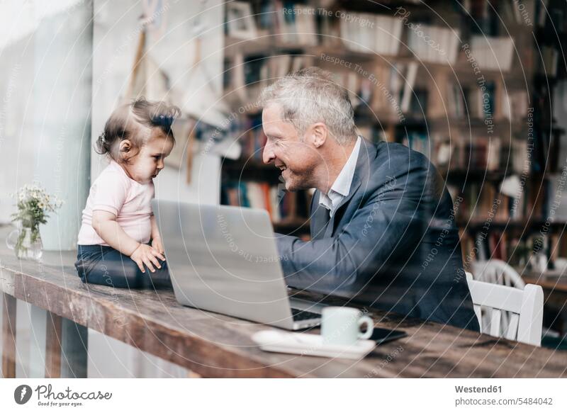 Businessman with little daughter working on laptop in cafe playing Laptop Computers laptops notebook sitting Seated father pa fathers daddy dads papa At Work