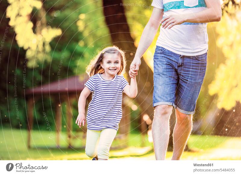 Portrait of smiling little girl running with her father hand in hand in a park fathers daddy dads papa daughter daughters parents family families people persons
