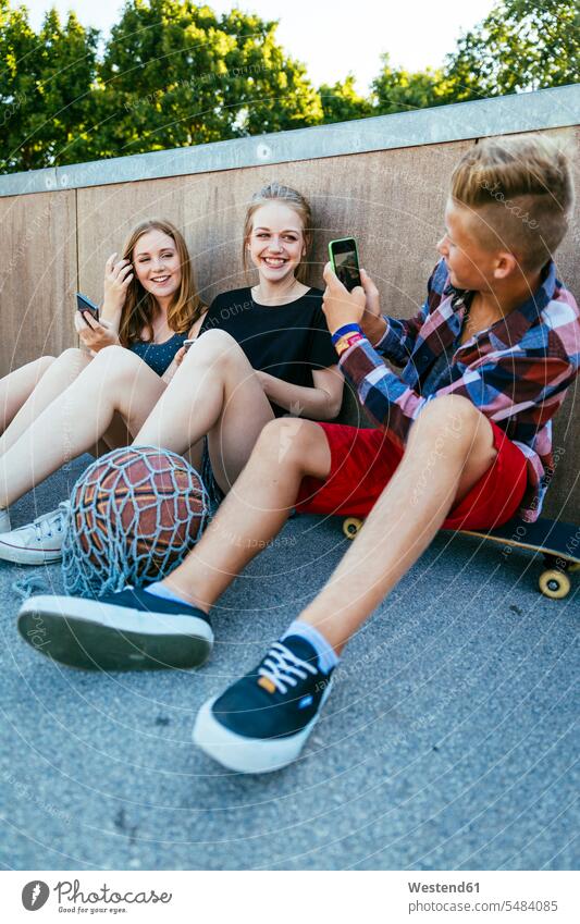 Teenage boy taking cell phone picture of friends outdoors skateboard Skate Board skateboards outdoor shots location shot location shots Smartphone iPhone