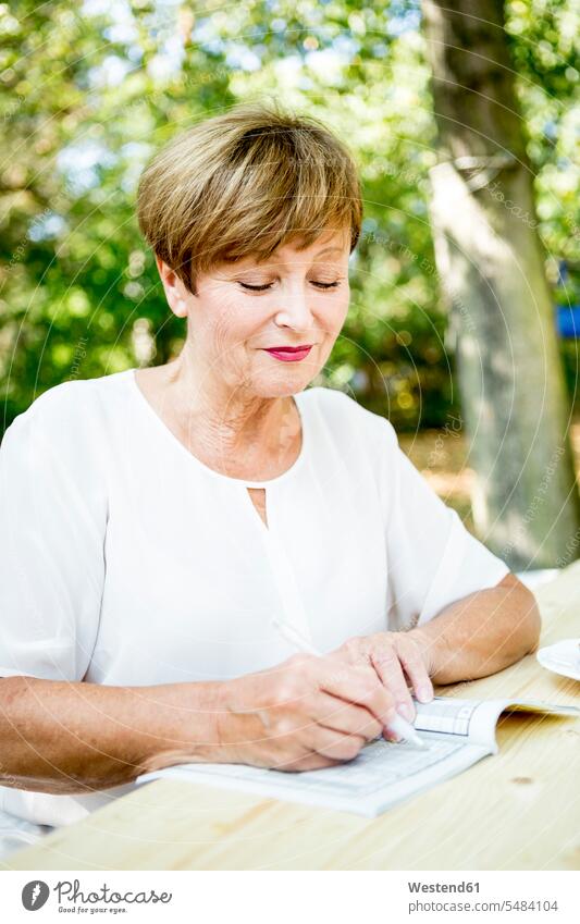 Senior woman doing a crossword puzzle outdoors Crossword females women smiling smile senior women elder women elder woman old senior woman Adults grown-ups