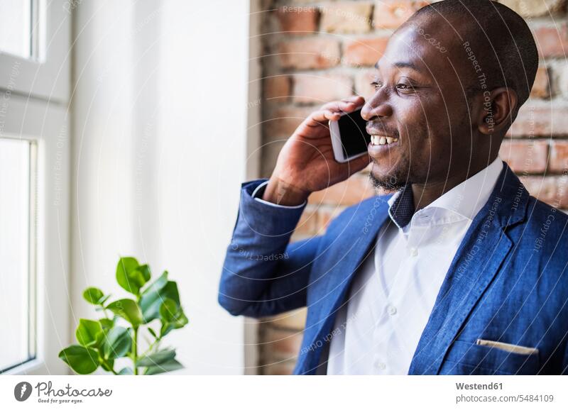 Smiling businessman on cell phone at the window mobile phone mobiles mobile phones Cellphone cell phones Businessman Business man Businessmen Business men