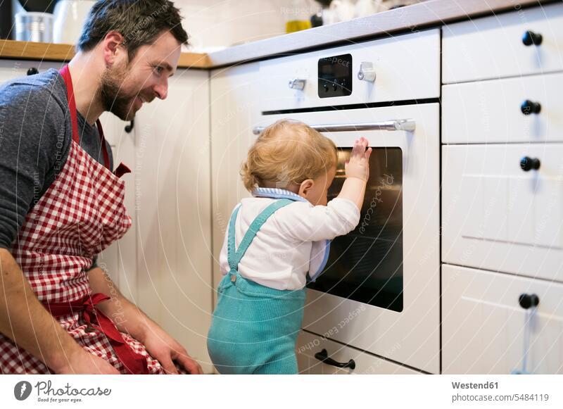 Father and baby boy in kitchen baking a cake son sons manchild manchildren oven pies cakes looking view seeing viewing bake father pa fathers daddy dads papa