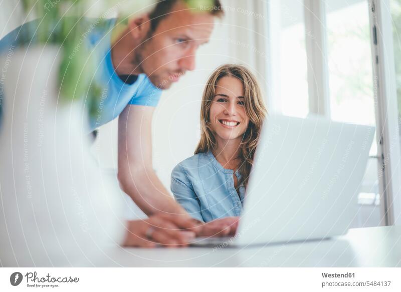 Smiling young woman and man using laptop at home couple twosomes partnership couples Laptop Computers laptops notebook home office working from home