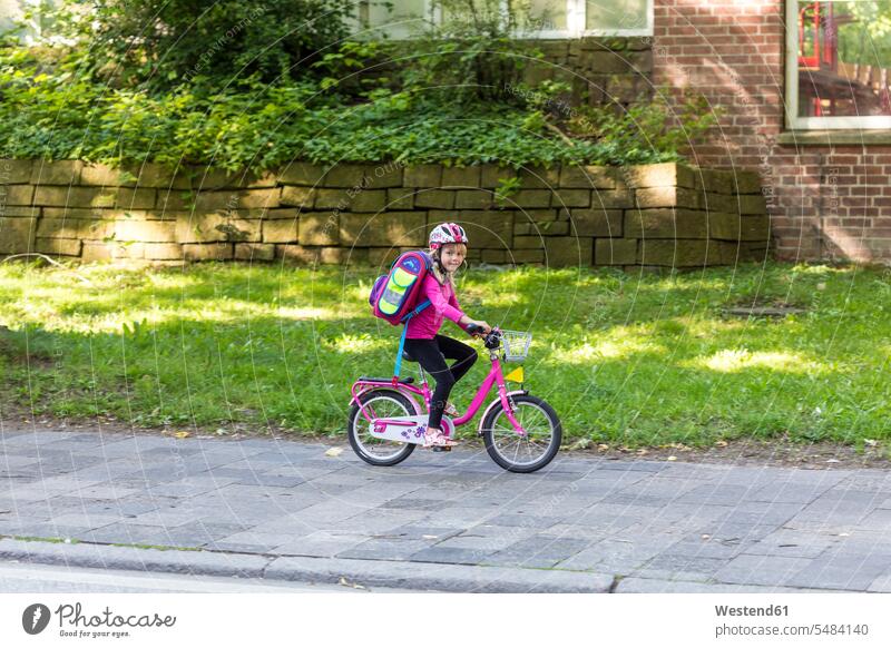 Smiling little girl with school bag riding bicycle on pavement riding bike bike riding cycling bicycling pedaling females girls Side Walk child children kid
