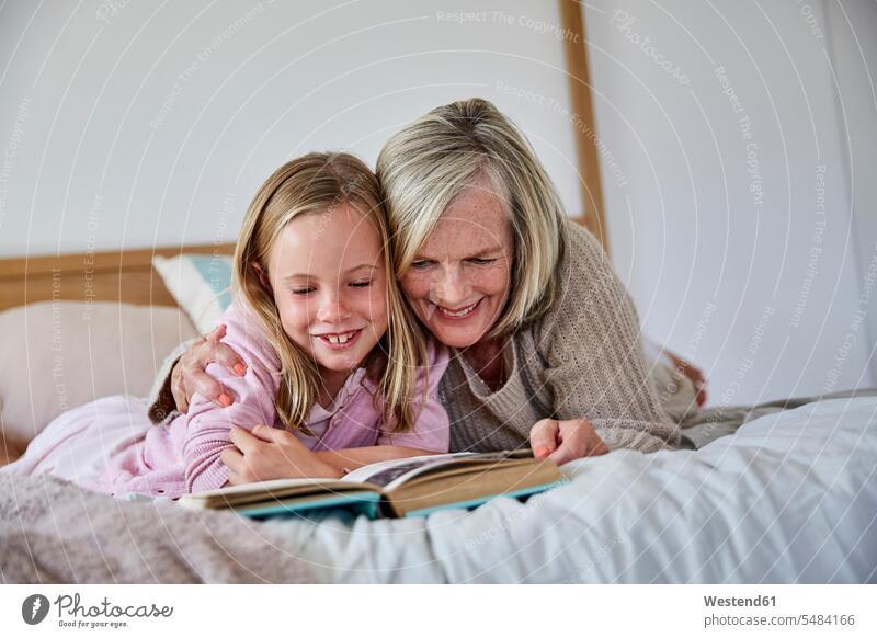 Little girl lying on the bed with her grandmother reading a book granddaughter granddaughters beds grandmas grandmothers granny grannies grandchild