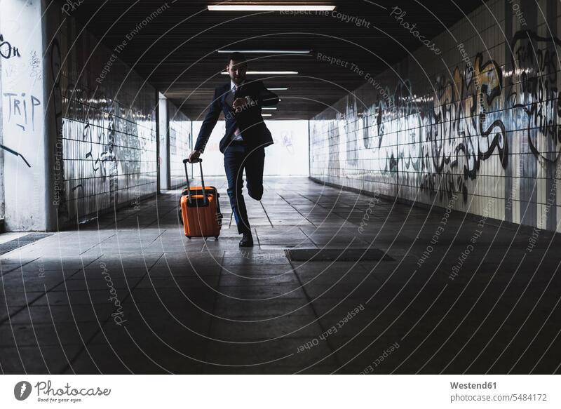 Businessman on business trip running with wheeled luggage tunnel Business man Businessmen Business men suitcase suitcases young transportation business people