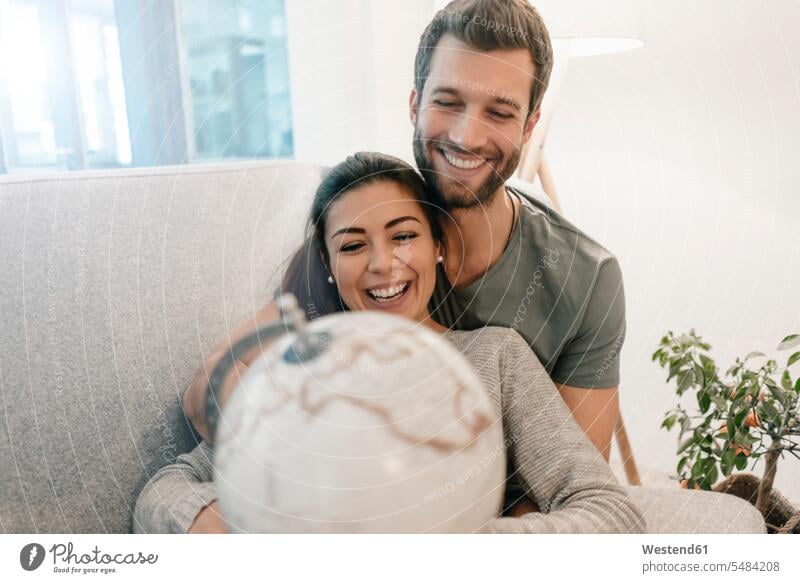 Happy couple on couch at home looking at globe relaxed relaxation twosomes partnership couples eyeing happiness happy settee sofa sofas couches settees globes