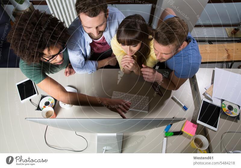 Team of creative professionals sitting around computer screen freelancer freelancing Small Business sharing share casual leisure wear casual clothing