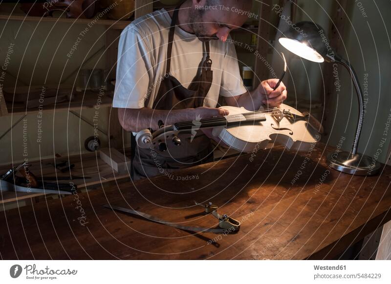 Luthier adjusting the sound post of a violin in his workshop man men males violins violin maker luthier working At Work Adults grown-ups grownups adult people