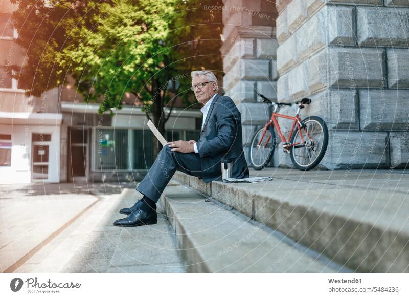 Senior businessman sitting on stairs, using laptop using a laptop Using Laptops working At Work Businessman Business man Businessmen Business men Seated online