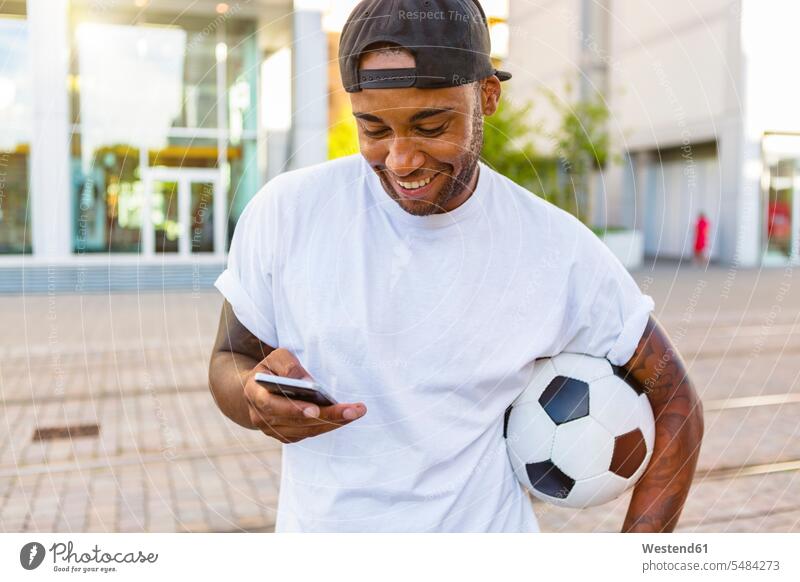 Laughing young man with soccer ball looking at cell phone Smartphone iPhone Smartphones soccer balls footballs men males mobile phone mobiles mobile phones