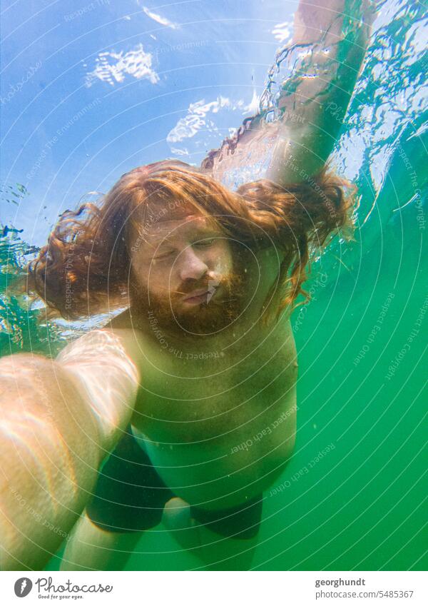 Man with red hair and red beard dives in a freshwater lake. Eyes open, but slightly squinted. He holds the camera. Lake underwater Dive be afloat bathe