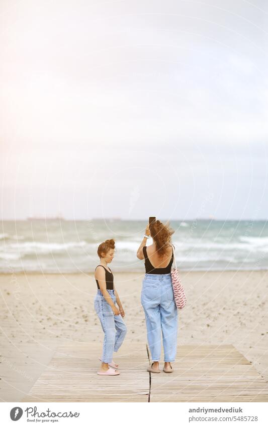 Happy family on beach vacation. Back view of mother and little daughter are walking together and holding hands on beach. Mom and child girl kid enjoy and having fun at summer holidays
