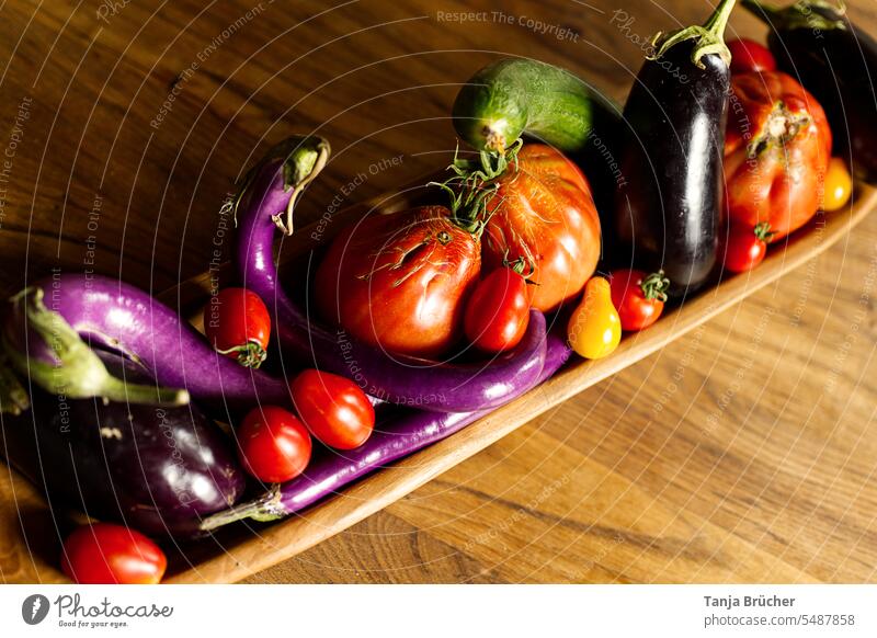 Various fresh vegetables in an oblong wooden bowl on grained wooden table Organic vegetables Vegetable tomatoes Tomato Aubergines elongated eggplants