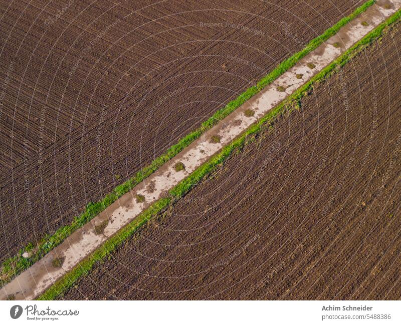Field path diagonally between fields with fertile land after the rain acre Arable land Aerial Shot extension concrete path Ground drone picture