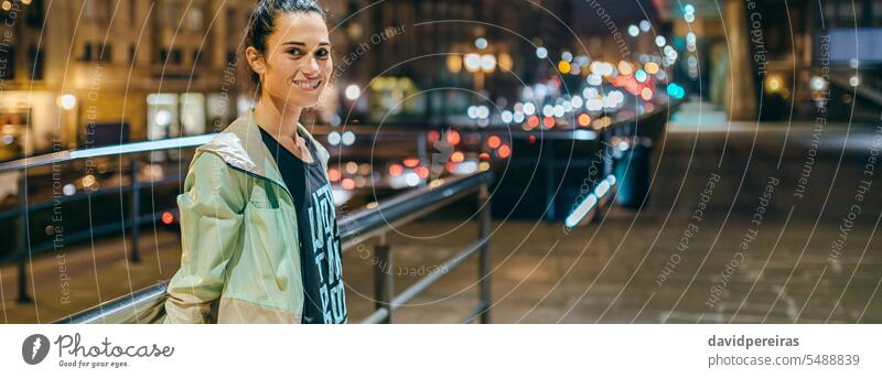 Woman wearing sportswear looking at camera with night town on background woman female runner portrait happy smile joy enjoy empty sidewalk city banner panoramic
