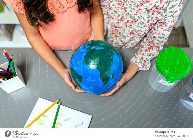 Two unrecognizable female students holding handmade globe world earth planet little girl school education sustainable ecologic global save concept map