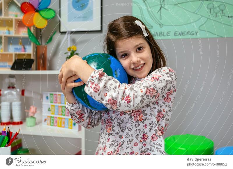 Female student hugging a handmade globe world at ecology classroom embracing earth planet female love little girl school smiling funny happy education