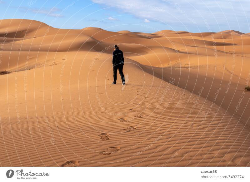 A person walking through the Erg Chebbi desert in the African Sahara hike alone symbol loneliness landscape sky blue dunes footsteps erg chebbi footprints