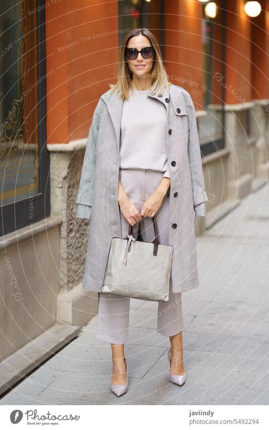 Confident stylish female standing on sidewalk woman businesswoman style pavement handbag coat high heels sunglasses formal street urban shop positive confident