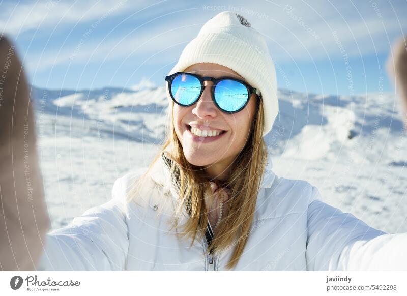 Cheerful woman in sunglasses taking selfie in snowy place winter mountain cold smile slope take photo adventure young female warm clothes happy nature outerwear