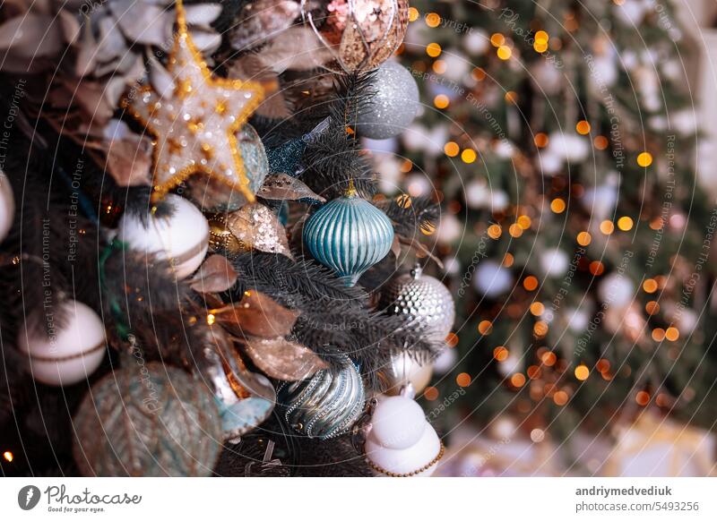 Close up view of glamour fir branches decorated with shiny silver and blue bauble or ball, star, xmas ornament and lights in decorated living room. Christmas holidays background. Festive new 2024 year