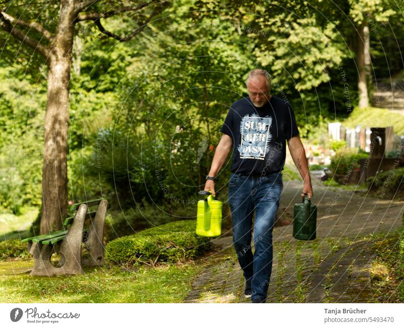 Man with two green watering cans on the way to water a grave at the cemetery middle-aged man 55 - 60 years 50 to 60 years 55 to 60 Mid adult man mature adult
