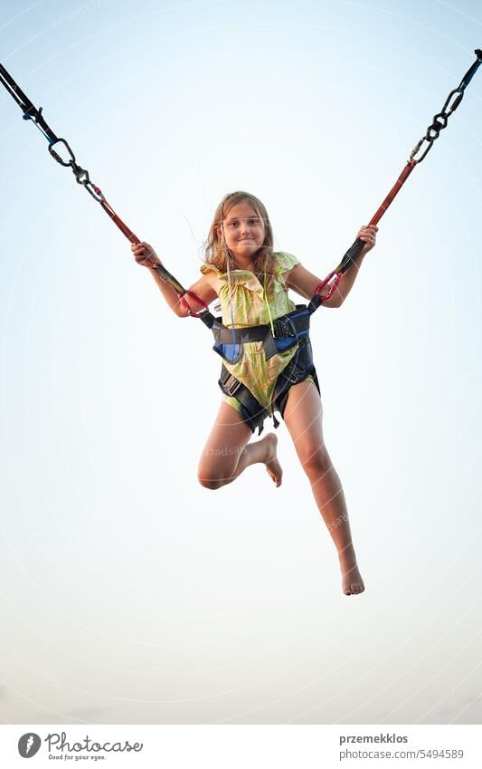Bungee jumping at trampoline. Little girl bouncing on bungee jumping in amusement park on summer vacations. Super girl playing person child fun activity sky