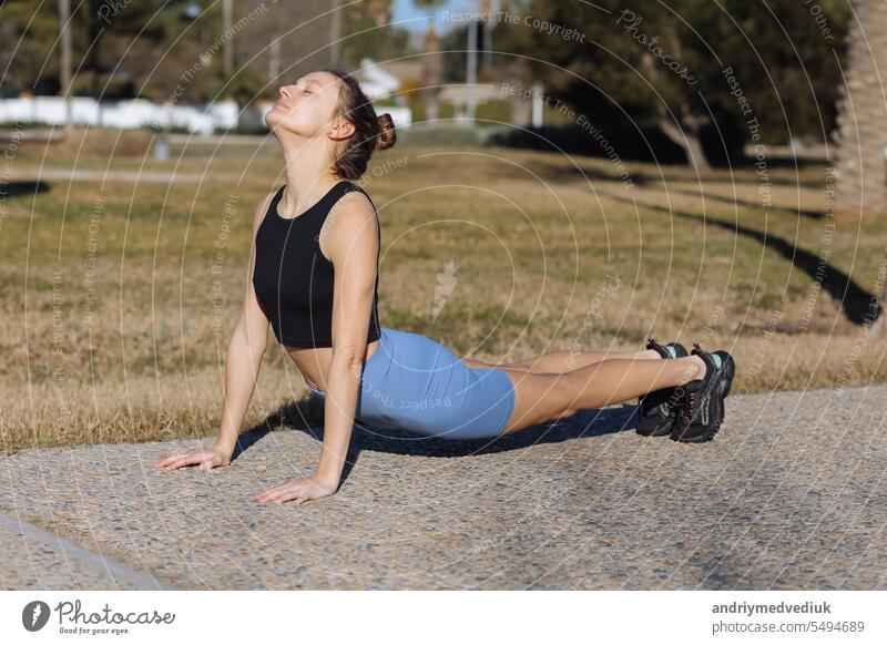 World health day. Beautiful fit young woman in sporswear working out outdoors at park, doing stretching exercises standing in pose dog muzzle up, sun salutation complex. Upward-Facing Dog Breakdown