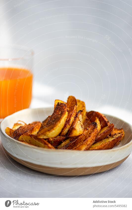 Fried potato with paprika spice served on ceramic plate near orange juice fried food drink glass table dish meal ingredient recipe yummy taste tasty eat dinner