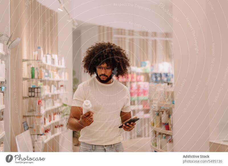 Black young man holding smartphone and reading product information from medicine bottle at pharmacy store buy customer drugstore confident online beard mobile