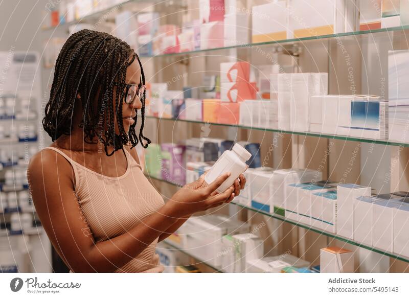 Black woman with dreadlocks reading label on bottle at pharmacy ingredient medicine drugstore buy customer package health care shop purchase information