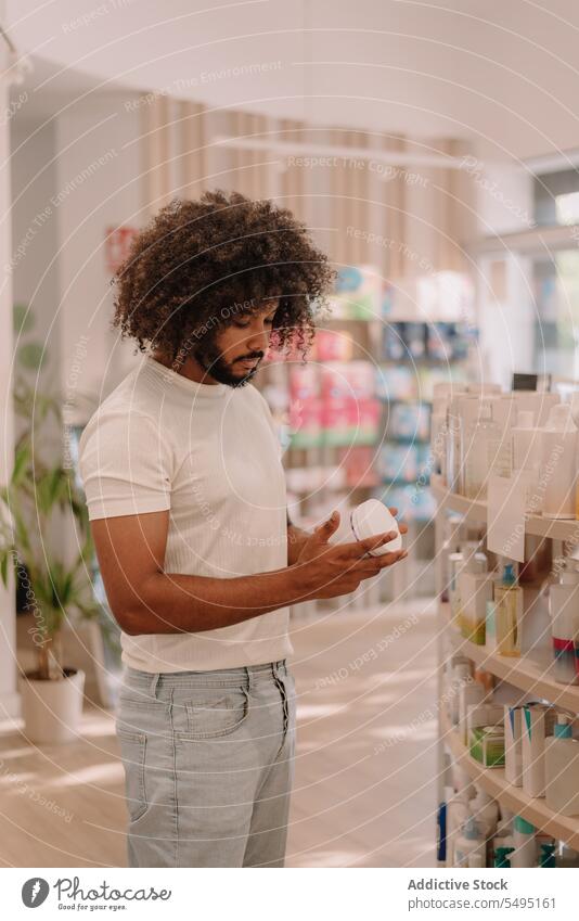 Black man with afro hairstyle reading label on bottle at pharmacy ingredient medicine drugstore buy customer package health care shop purchase information