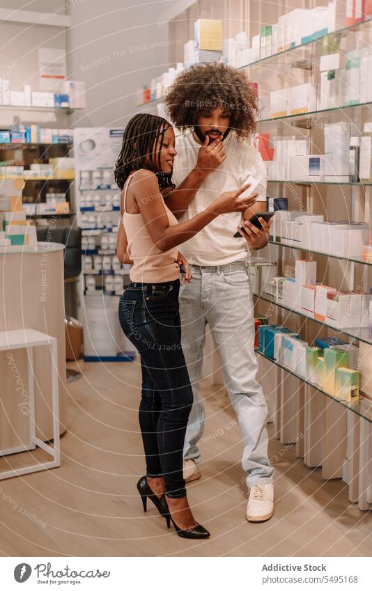 Black couple reading information on cellphone at drugstore boyfriend girlfriend pharmacy buy man woman smartphone medicine bottle package health care shop