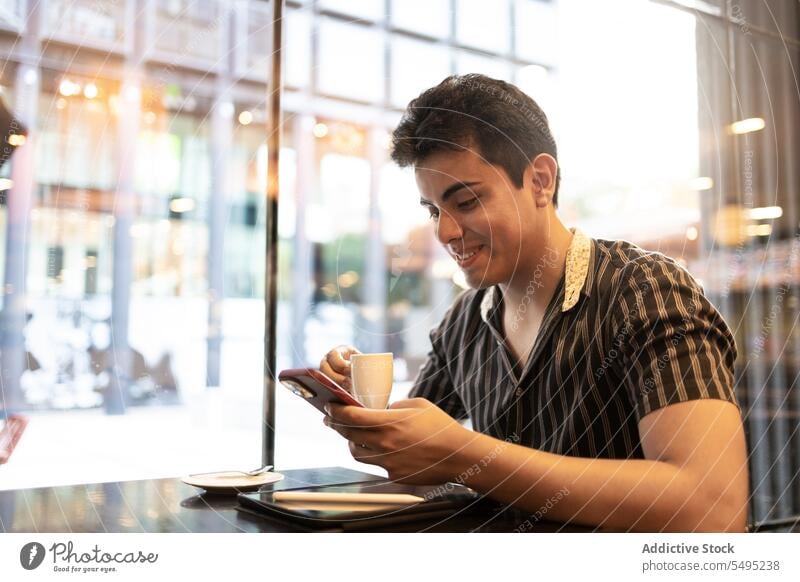 Man holding coffee cup and using smartphone in cafes man smile young sitting window digital tablet lifestyle mobile hot drink handsome casual attire happy