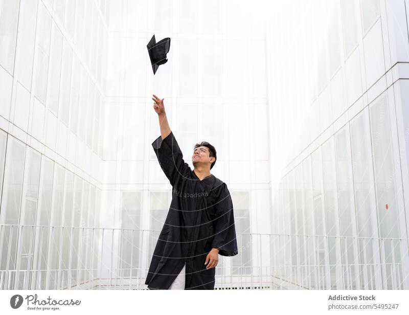 Man in graduation gown throwing mortarboard in air student cap mid-air cheerful man education achievement happy black smile celebration hand raised standing